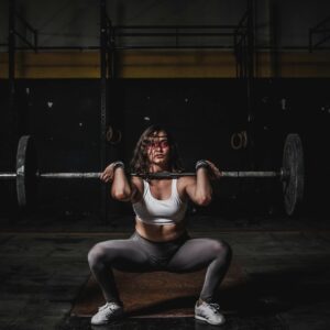 A strong female weightlifter squats with a barbell in a dimly lit gym, showcasing power and fitness.