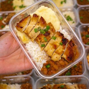 Delicious grilled chicken meal with rice, beans, and mashed potatoes in a meal prep container.